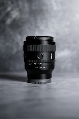 A moody, dark-toned photo of a camera lens resting on a sleek black surface, hinting at creative focus.