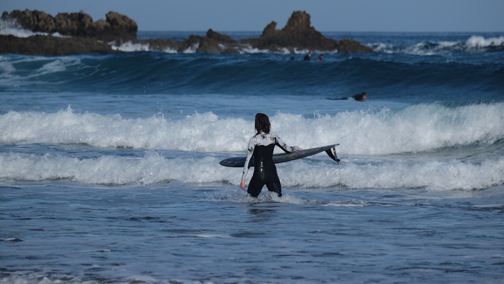 a woman holding a surfboard walking into the ocean