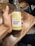 A hand is holding a glass bottle of sparkling kombucha labeled 'umami brew' with a 'Pineapple Spice' flavor. The bottle is displayed against a wooden table surface. A glass filled with a beverage is visible in the background.