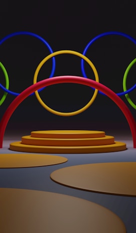 A series of interlocking rings in vibrant primary colors are suspended in front of a platform composed of circular steps. The colors include red, blue, green, and yellow, creating a visually engaging and vivid design against a dark background.