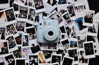 A collection of various instant photographs spread out on a surface with a light blue instant camera placed in the center. The photographs capture different scenes and people, featuring portraits, outdoor settings, and candid moments. The arrangement is casual and slightly overlapping.
