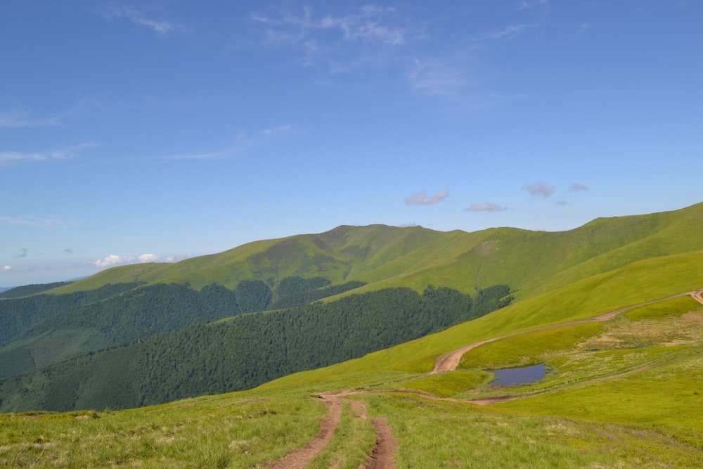 a dirt road on a grassy hill with mountains in the background