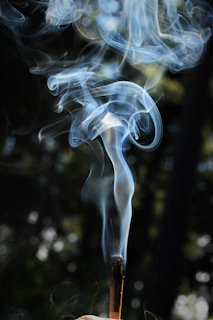 An artistic shot of golden bakhoor smoke swirling above an ornate incense burner against a black background with subtle gold accents.