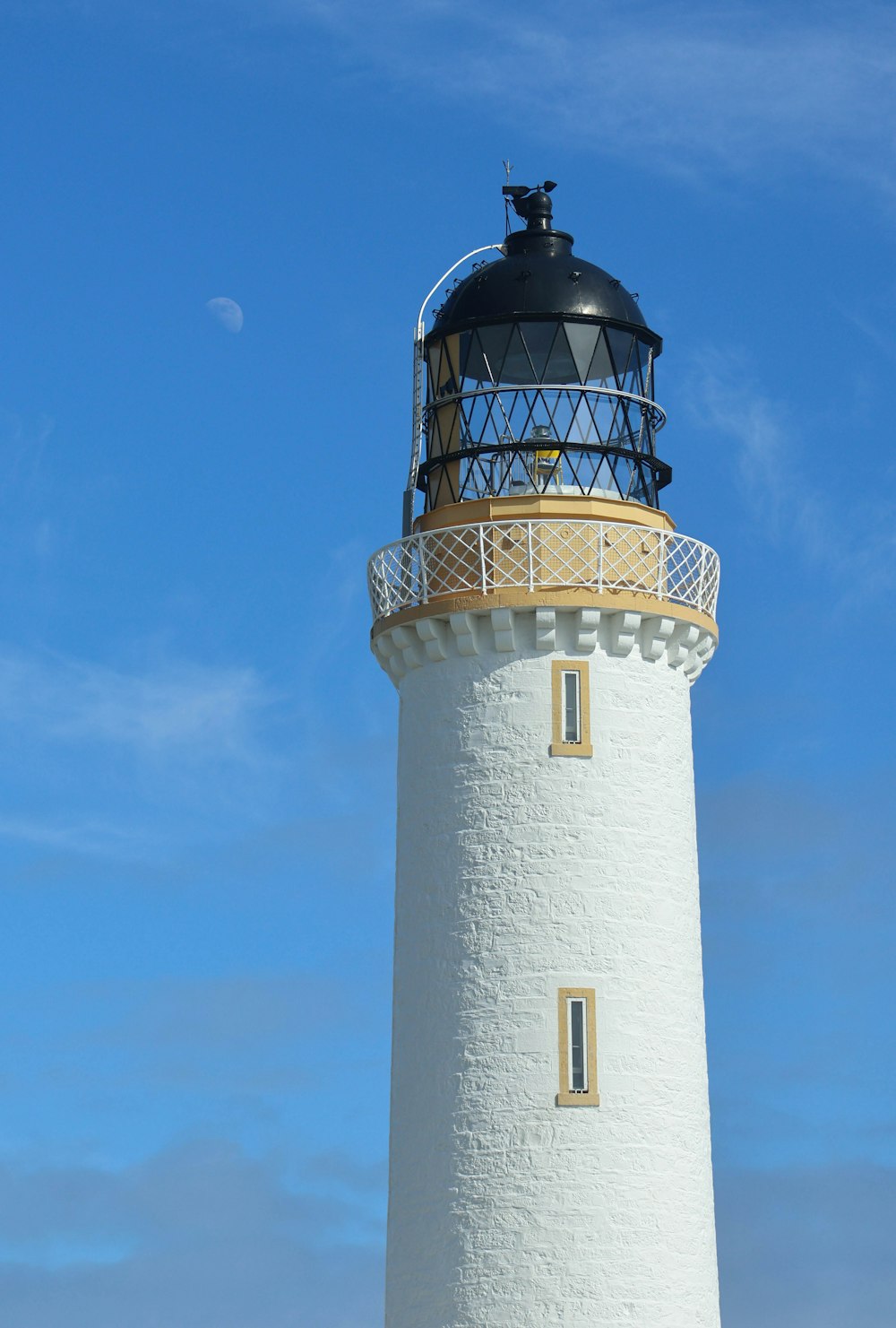 a white and black lighthouse with a blue sky in the background