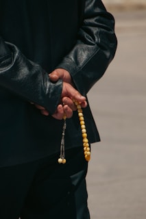 a man in a black jacket holding a yellow beaded rosary