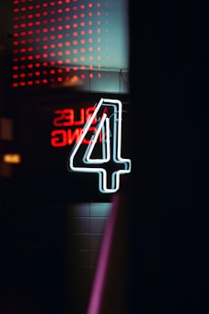 A holographic nyx4 logo glowing neon cyan against a rain-soaked cyberpunk cityscape at midnight.