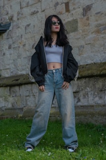 Model wearing a stylish jacket and jeans standing against a brick wall backdrop