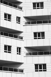 Multiple balconies with glass railings and a modern design style, featuring clean lines and grid patterns. The surface material appears to be a white or light-colored panel.