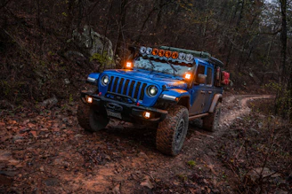 Off-road vehicle equipped with bright auxiliary LED lights illuminating a forest trail at night.