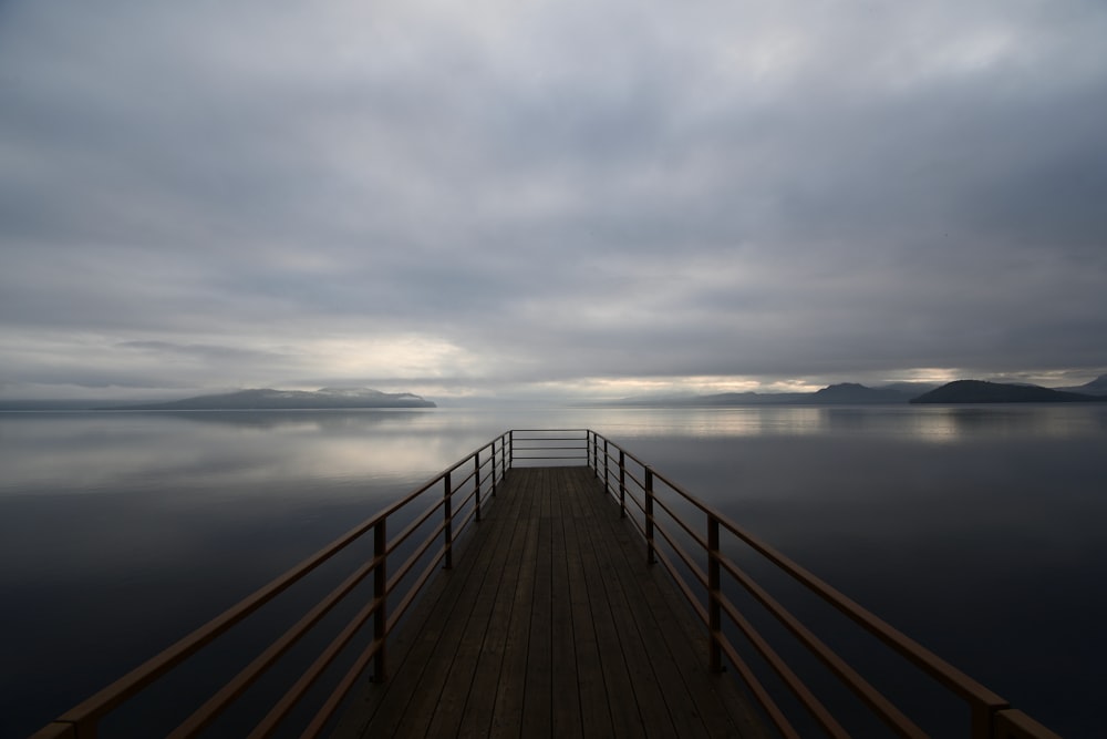 a wooden dock sitting on top of a lake under a cloudy sky