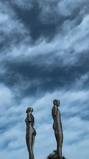 Outdoor installation of intertwined metal figures against a blue sky