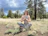 A peaceful man sitting outdoors with eyes closed in prayer, surrounded by nature.