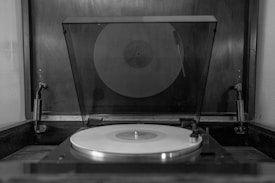 A vinyl record is spinning on a vintage turntable, enclosed by a transparent dust cover. The setup is situated within a wooden casing, providing a classic and nostalgic atmosphere.