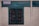 A rustic, weathered wall made of light-colored bricks contains a central window with a green frame. The window features mesh grids. Above, a small sign indicates information about painting classes organized by a women's conference.
