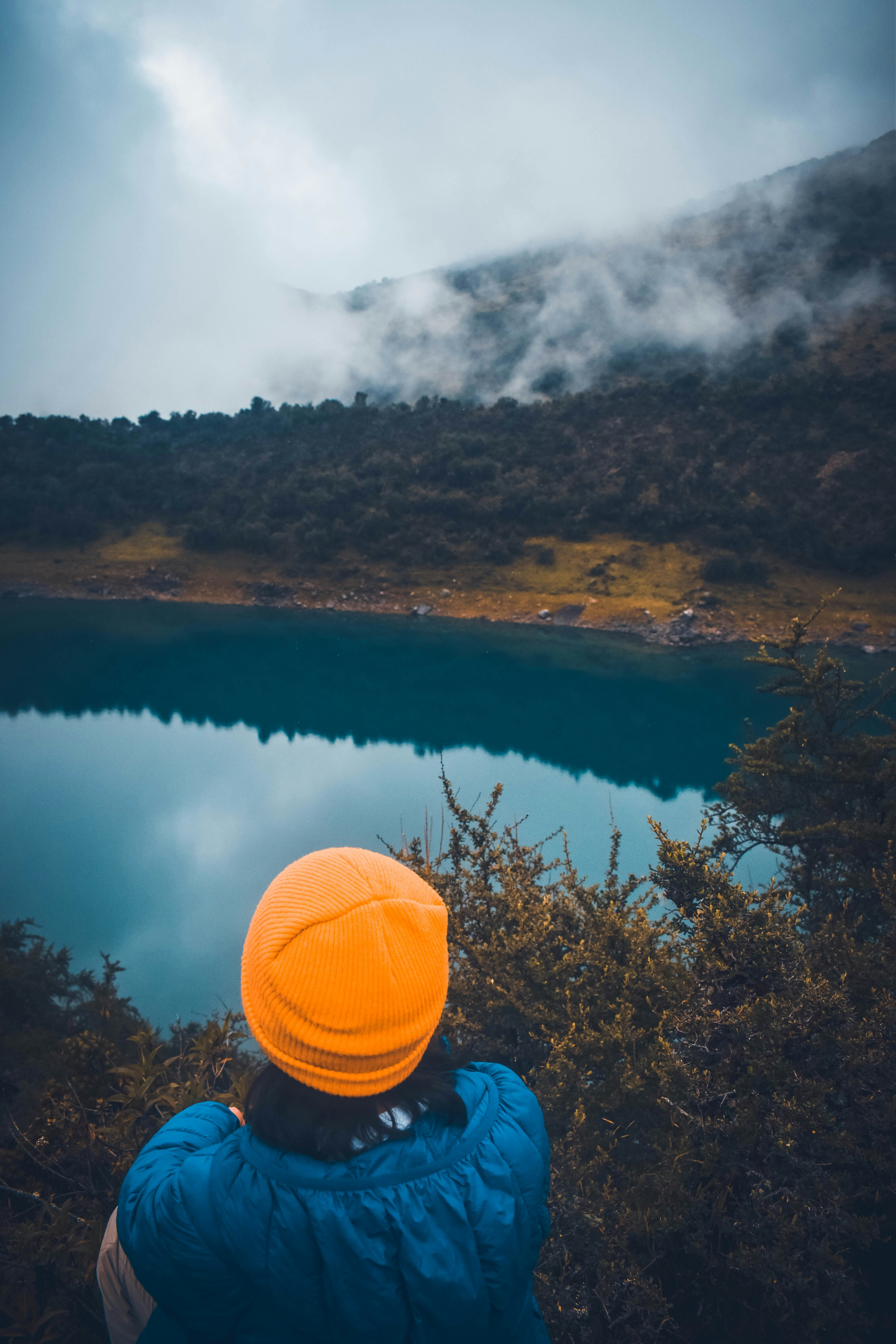 a person in a blue jacket and orange hat looking at a lake