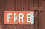 A weathered sign with the word 'FIRE' in bold white letters on a red background is attached to a rustic wooden surface. The sign is peeling and shows signs of aging, with some of the paint chipped away.