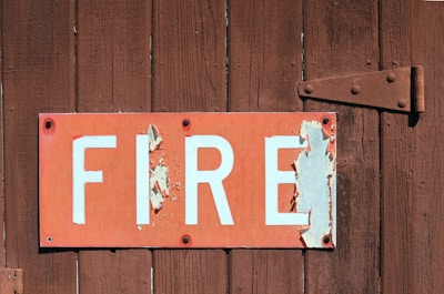 A weathered sign with the word 'FIRE' in bold white letters on a red background is attached to a rustic wooden surface. The sign is peeling and shows signs of aging, with some of the paint chipped away.