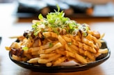 a plate of french fries with sauce and sprouts