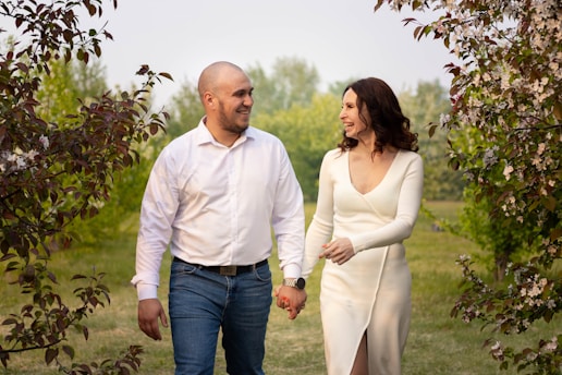 A couple holding hands while walking through a sunlit park, surrounded by blooming flowers.