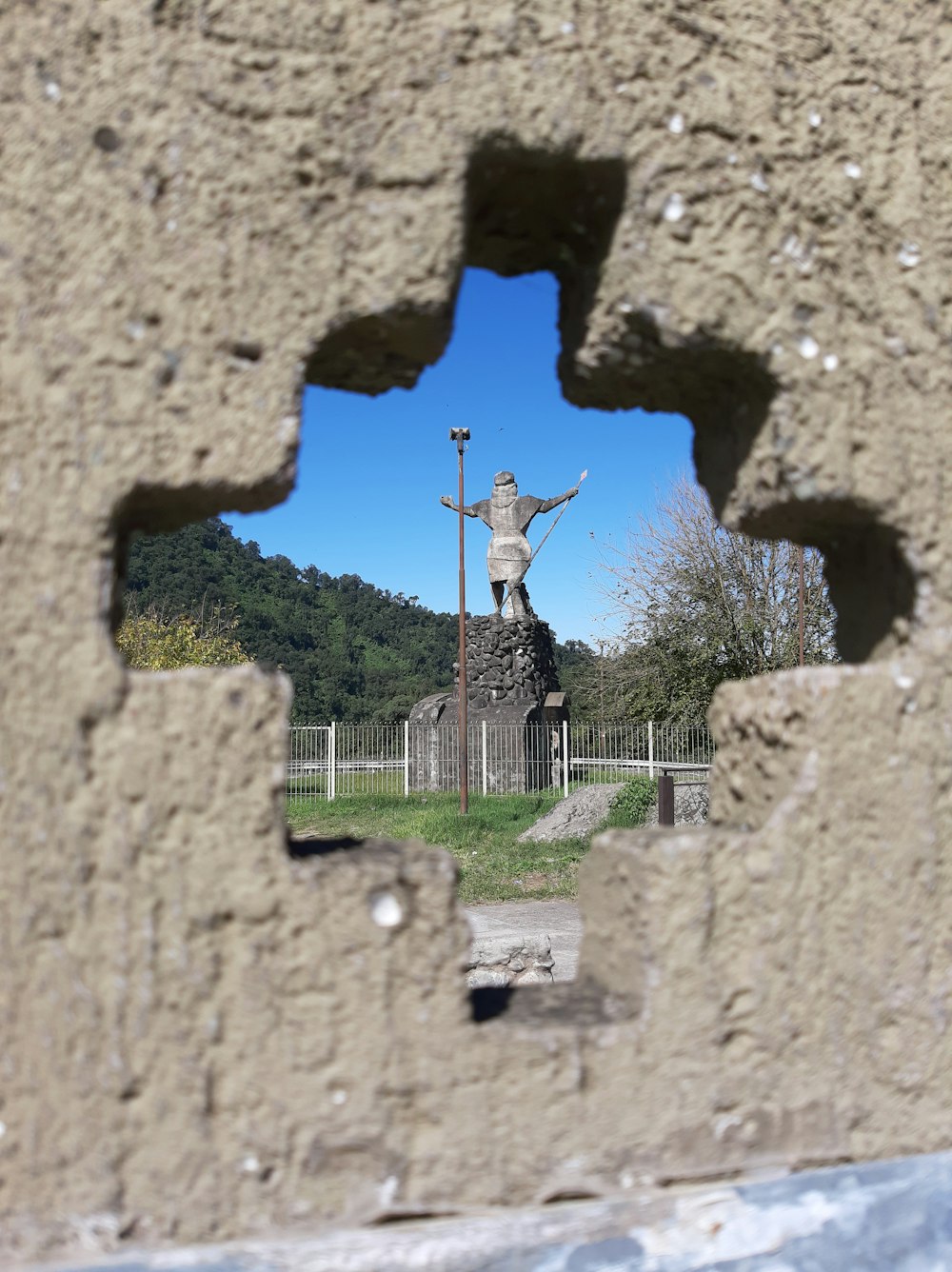 a hole in a stone wall with a statue in the background