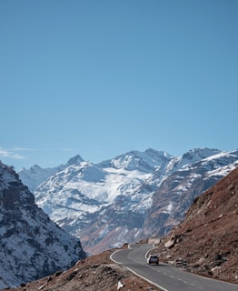a car driving down a mountain road with snow covered mountains in the background