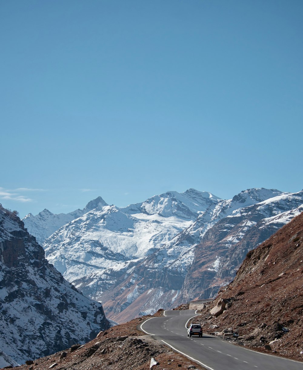 a car driving down a mountain road with snow covered mountains in the background