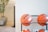 Several basketballs are neatly stored on a metal rack against a plain white wall. A potted plant is slightly visible in the blurred background, creating a casual and organized environment.