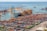 Numerous colorful shipping containers neatly arranged in a large port area near the ocean. Several large cranes are present, indicating an active shipping or logistics hub. The vast expanse of the sea in the background highlights the scale of the port.