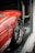 A red sports car is securely fastened inside a trailer. The focus is on the rear section, highlighting the sleek metallic wheel and tire. Visible branding and sponsor logos add a racing aesthetic to the scene.