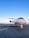 A sleek white private jet is parked on an airport runway under a clear blue sky. The aircraft's nose is prominently visible, highlighting its streamlined design. The background shows an expansive view of the runway, stretching out with no obstructions.