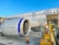 A large airplane on the tarmac, with a close-up view of its engine and baggage being loaded onto the aircraft. The airplane has a Scandinavian airline logo, and the sky is clear and blue.