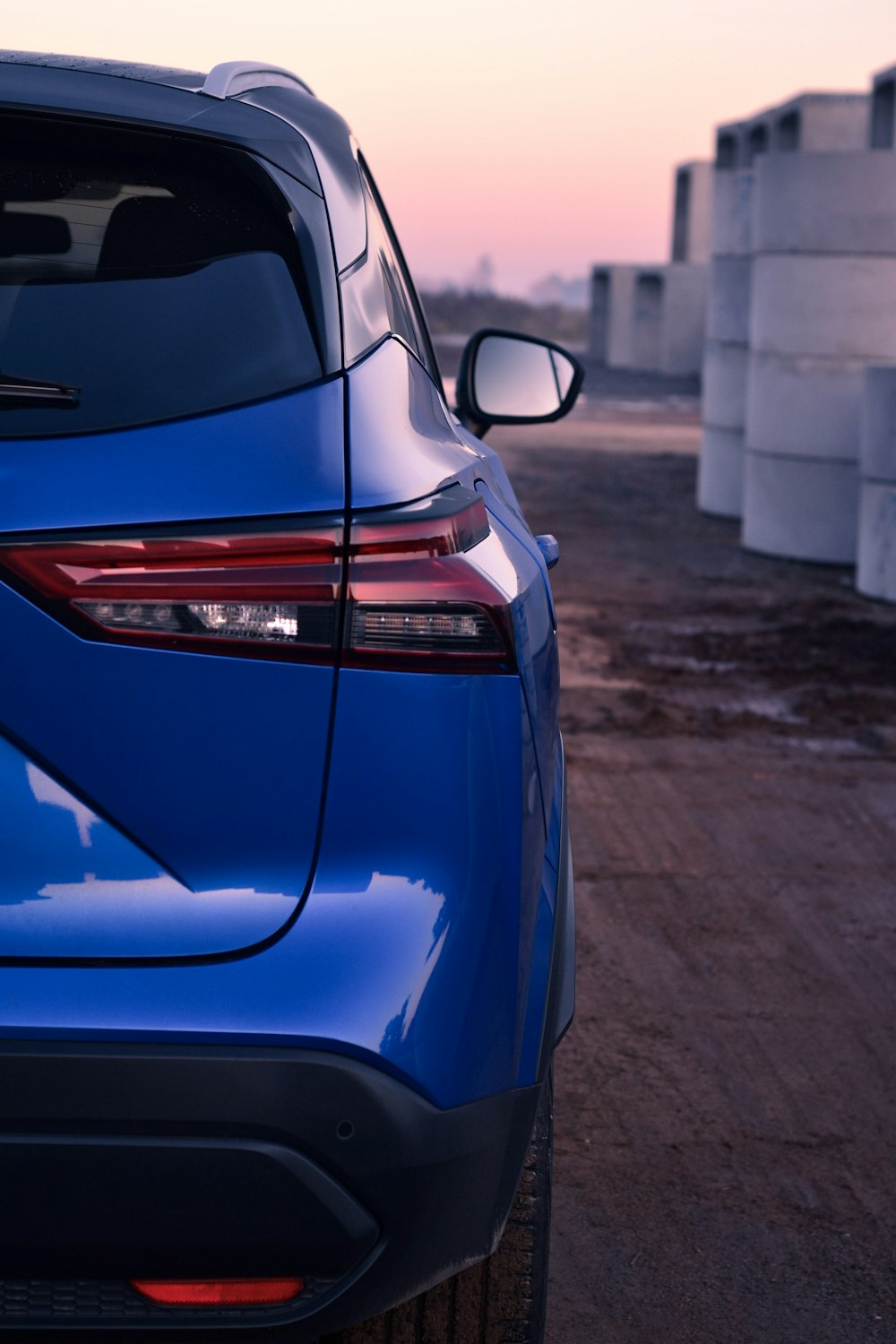 the rear end of a blue car parked on a dirt road