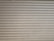 A series of horizontal metal slats form a shutter or garage door, featuring a light gray color with various small marks and stains across its surface.