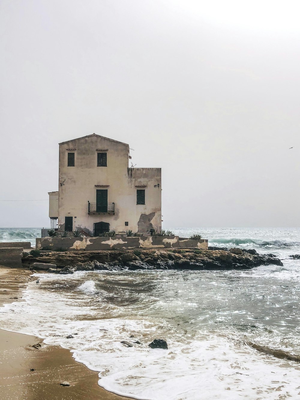 an old building sitting on top of a beach next to the ocean