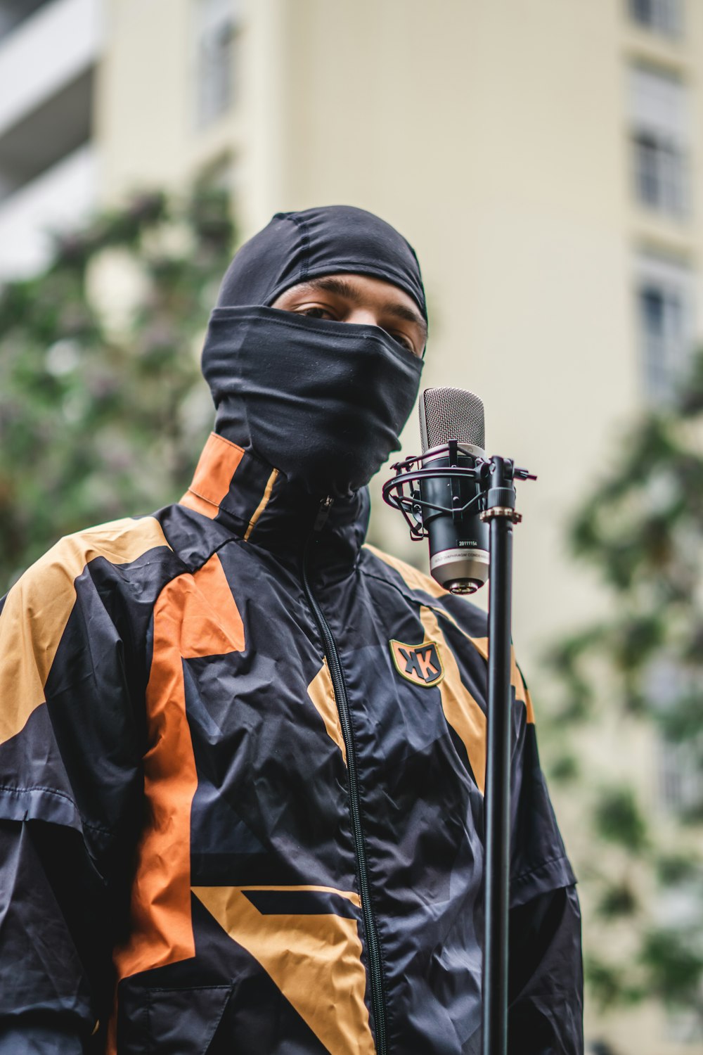 a man in a black and orange jacket holding a microphone