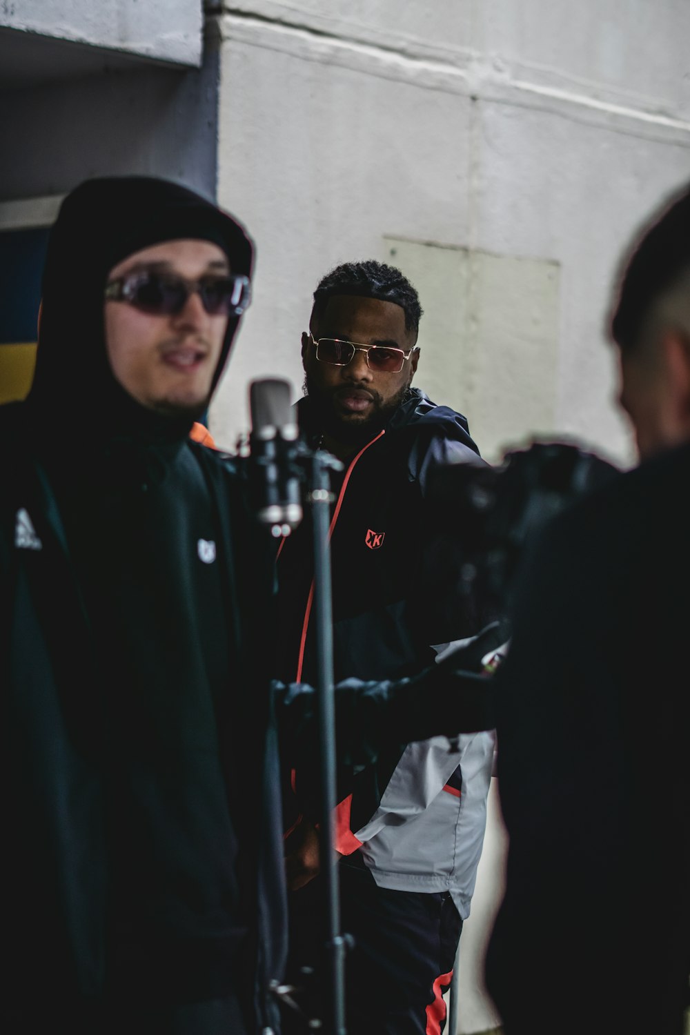 a man in a black hoodie and sunglasses standing next to a microphone