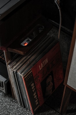 A collection of vinyl records stored upright with a prominent album cover featuring the word 'LATIN' and an illustration of a woman's face. The scene is dimly lit, and there's an electronic device and a power strip nearby.