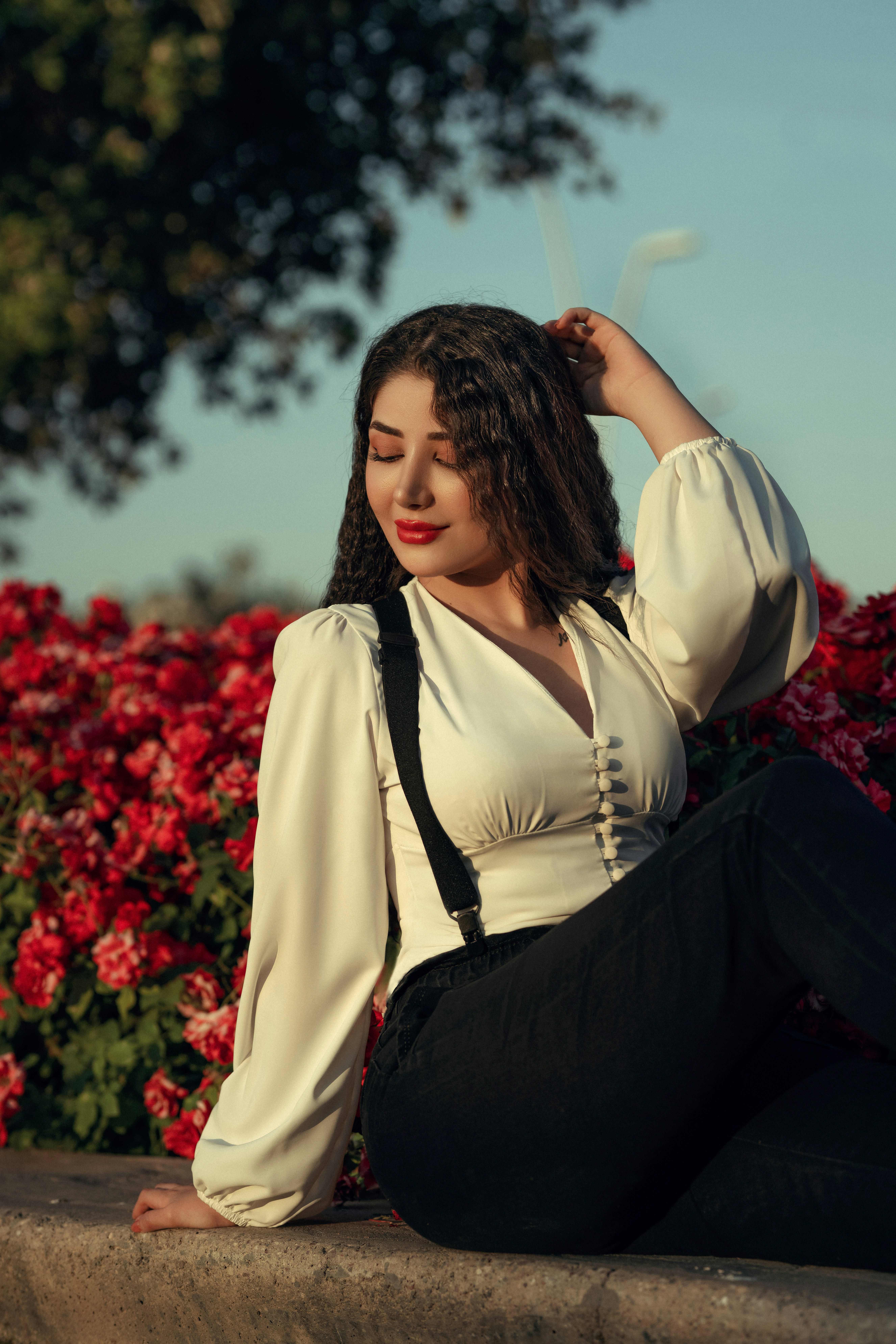 한 여자가 꽃을 배경으로 벽에 앉아 있다