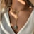 A close-up of a delicate gold necklace on a soft fabric background.