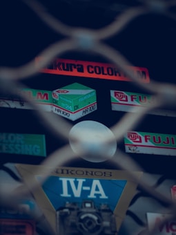 A selection of vintage film and camera gear is visible behind a metal fence, featuring branding like Fuji and Nikonos. The overall scene has a retro, nostalgic feel.