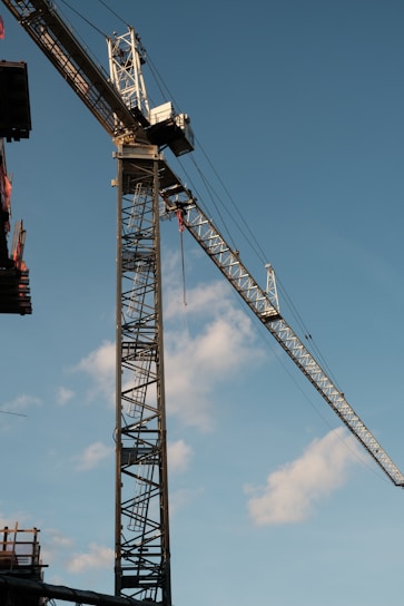 Tower crane securely lifting heavy steel beams at a bustling construction site under clear skies.