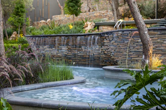 A serene backyard garden featuring a minimalist water feature and tropical foliage.