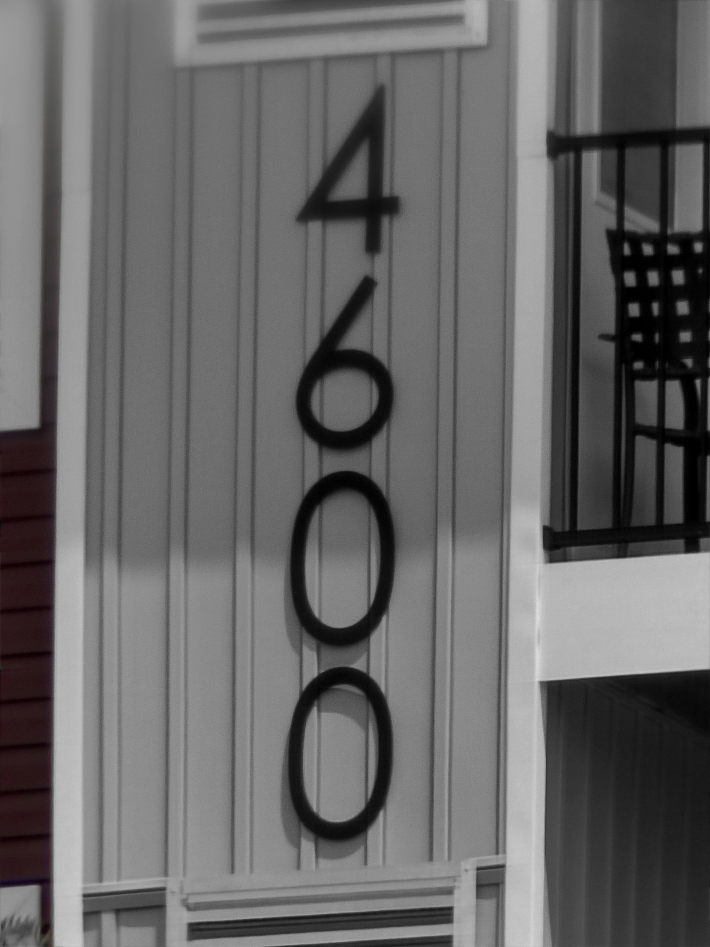 Tall vertical numbers on a light siding panel mark a building entrance; architectural details include a balcony railing shadow and a doorway edge.