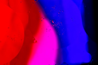 Colorful abstract pattern with vibrant red, pink, and blue hues blending together. Tiny bubbles or droplets are scattered across the surface, adding texture and depth.