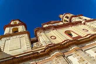 A detailed architectural view of a historic building showcasing intricate designs and patterns. The structure features ornate columns, arches, and richly textured stonework under a clear blue sky.