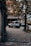 A rugged SUV is parked on a cobblestone driveway in front of a hotel with a classic European facade. Lush greenery, including trees with dense leaves, frames the scene, and soft, diffused lighting suggests an overcast day.