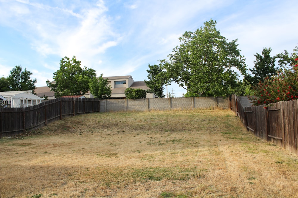 an empty yard with a fence and a house in the background