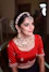 a woman wearing a red blouse and gold jewelry