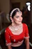 a woman wearing a red blouse and gold jewelry