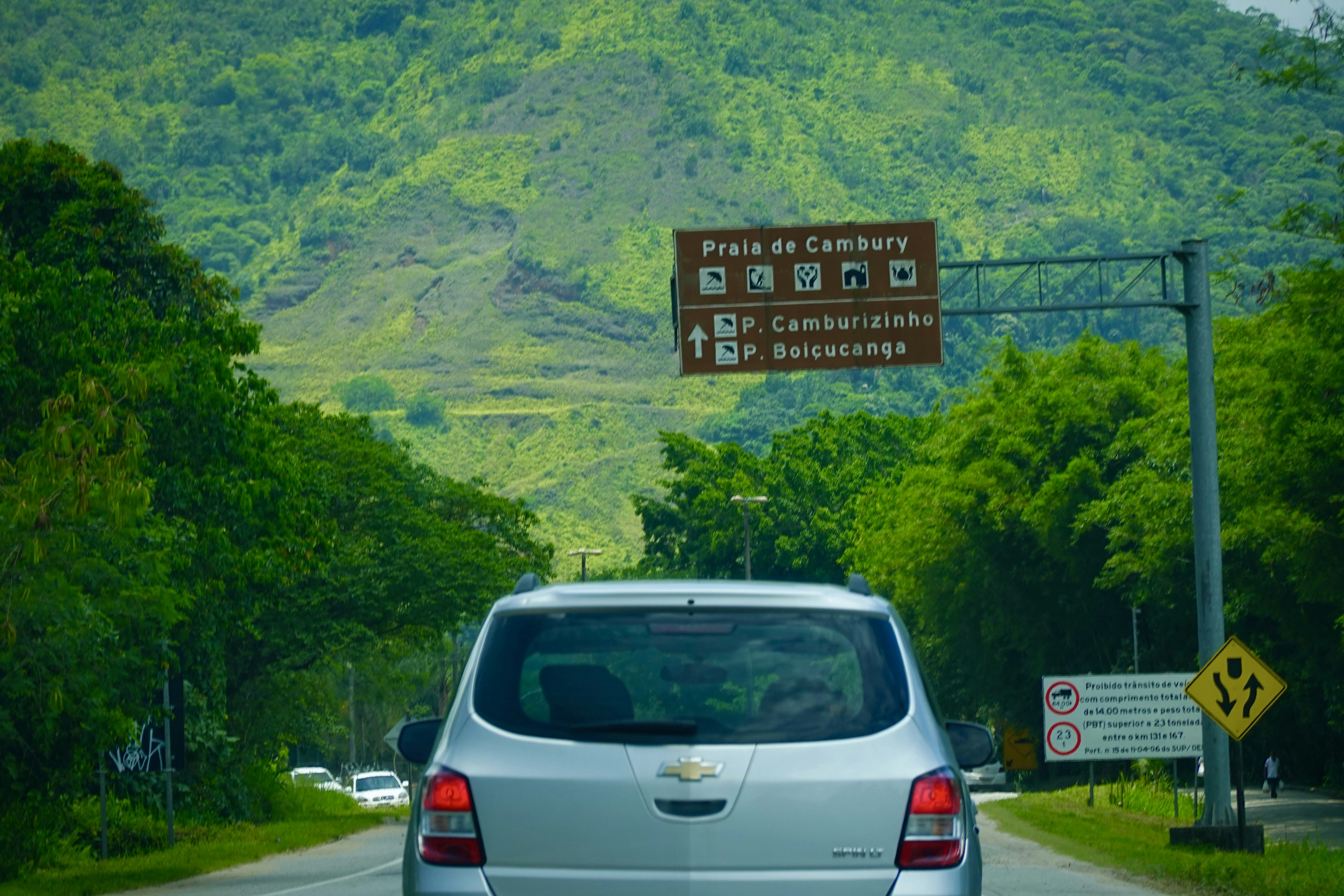 a silver car driving down a road next to a lush green hillside